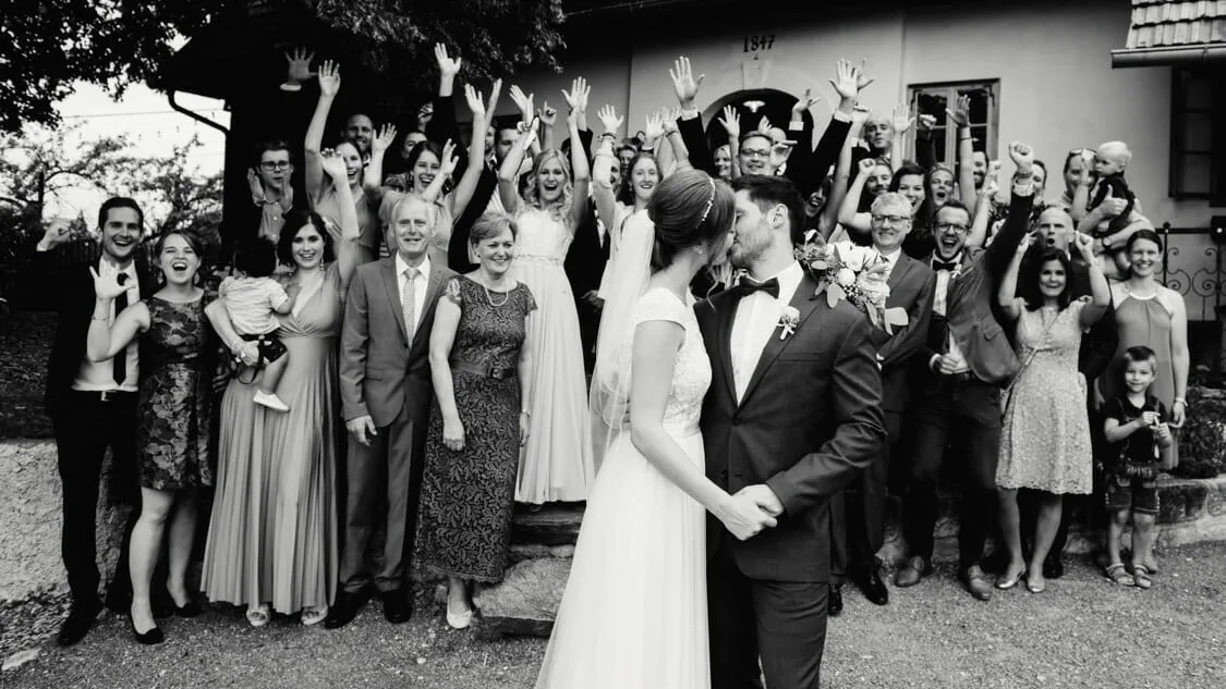 Alexandra und David mit ihren jubelnden Gästen am Knappenhof, in Schwarz-Weiß